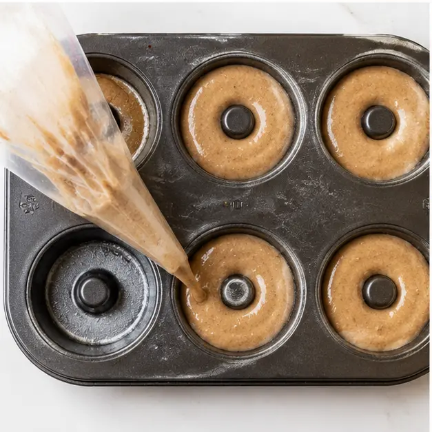 Piping batter into a greased donut pan