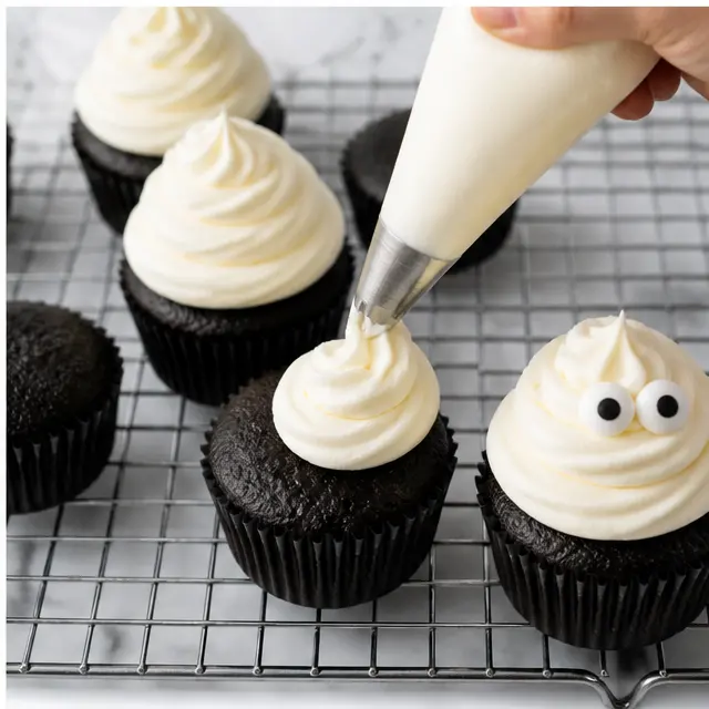 Piping ghost swirls and adding candy eyes to the finished cupcakes