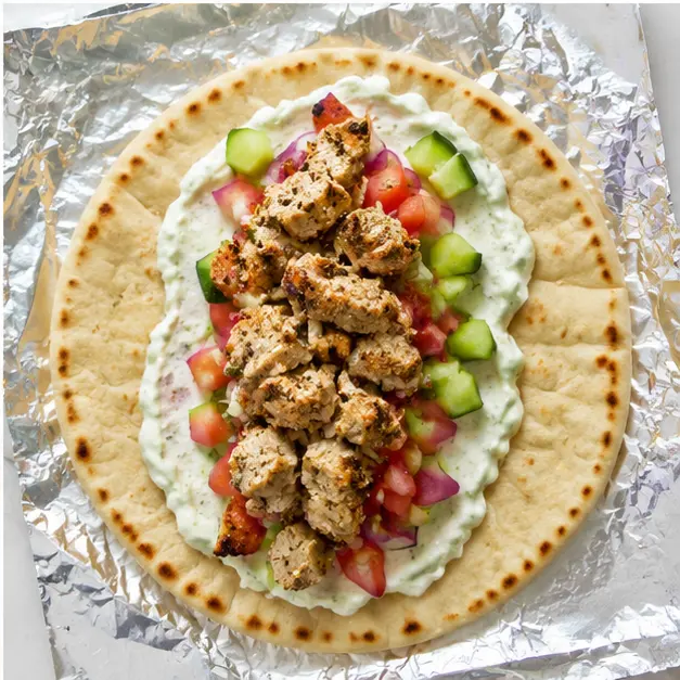 Assembling gyros with tzatziki, veggies, and chicken