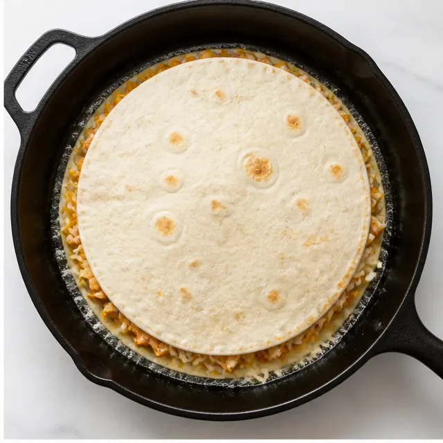 Layering shredded cheese and chopped chicken over the sauce