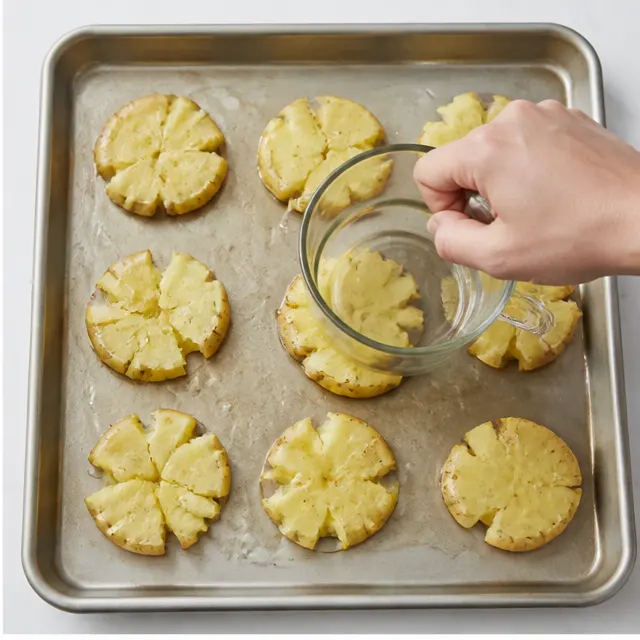 Step 2: Smashing warm boiled potatoes flat with a measuring cup on an oiled baking sheet