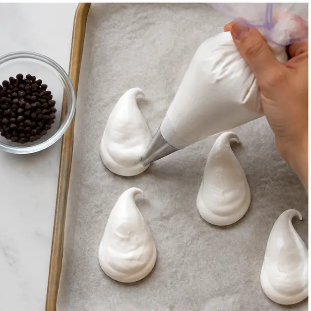 Piping ghost shapes from a plastic bag onto parchment paper