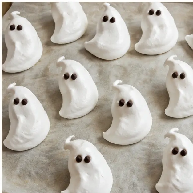 Baked crisp ghost meringue cookies cooling on parchment paper