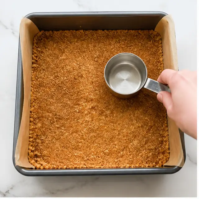 Pressing the spiced molasses graham cracker crust into the parchment-lined 9x9 pan