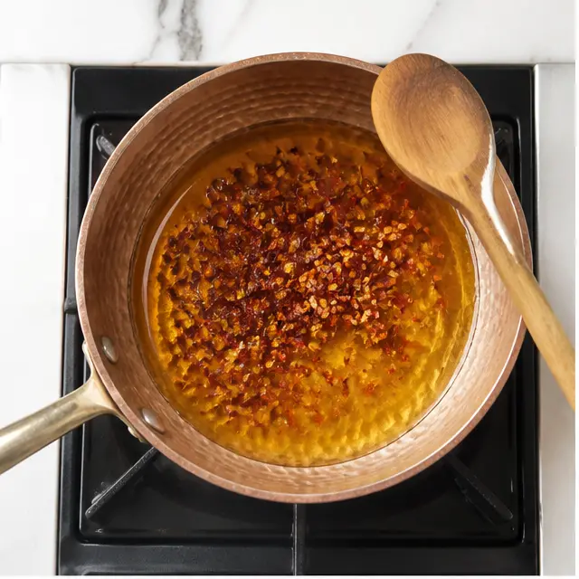 Step 1: Warming honey and crushed red pepper flakes together in a copper saucepan over medium-low heat