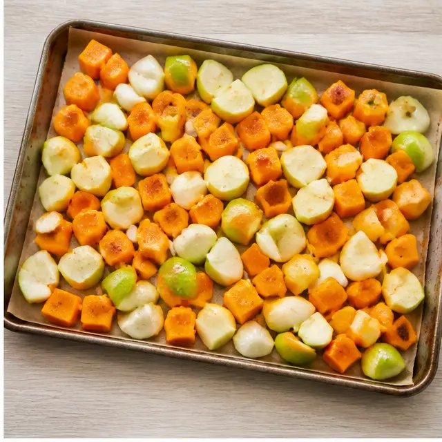 Tossing cubed butternut squash, apple, and onion in olive oil on a sheet pan