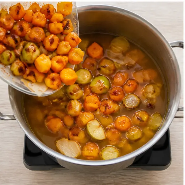 Simmering roasted vegetables with chicken broth in a large pot on the stovetop